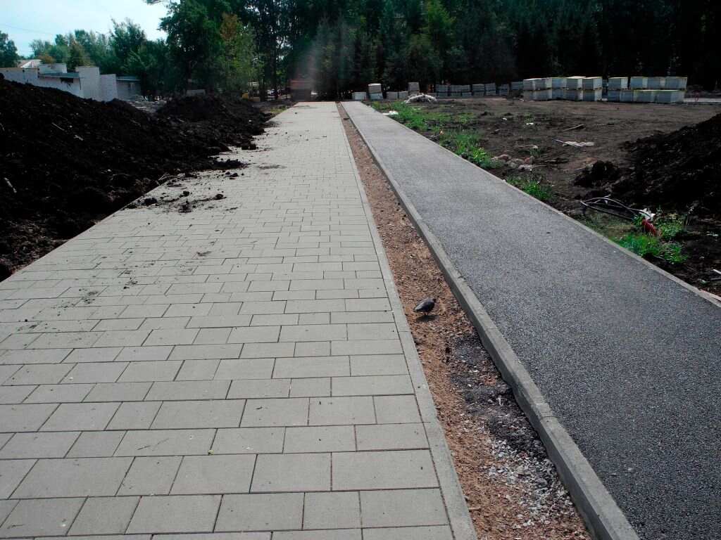 Workers smoothing a concrete sidewalk made of cement and brick, with tools arranged neatly around the site